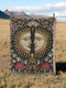 Jacquard-woven cotton blanket featuring twin celestial suns—two serene faces meeting at center—with radiant golden rays on a charcoal ground, bordered by folkloric botanicals and fan blossoms in sage, sky, and garnet. Crafted from 100% soft cotton yarn; the artwork is woven, not printed. Reversible with a color-negative back and finished with a protective 2-inch multicolor fringe. Sizes: 52×37, 50×60, 60×80 for wall, sofa, or queen-bed layering.